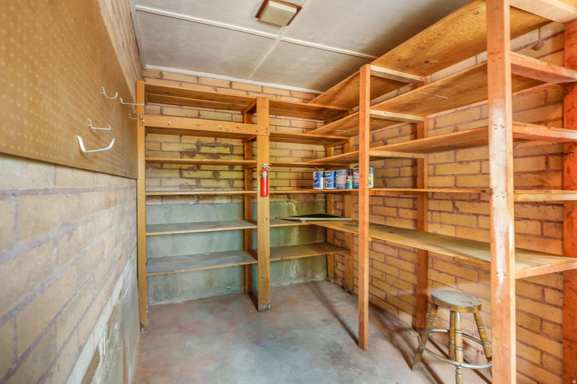 Brick wall construction with extensive built-in wood shelving, a concrete floor, and a pegboard wall