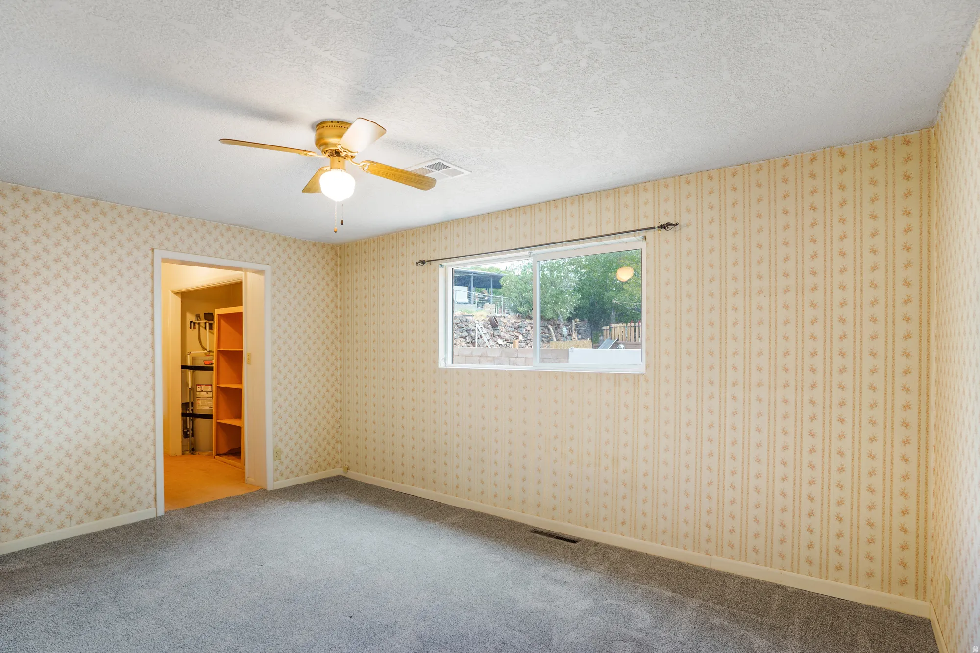 Wall-to-wall carpeting with patterned wallpaper, a single window, and a ceiling fan with integrated lighting