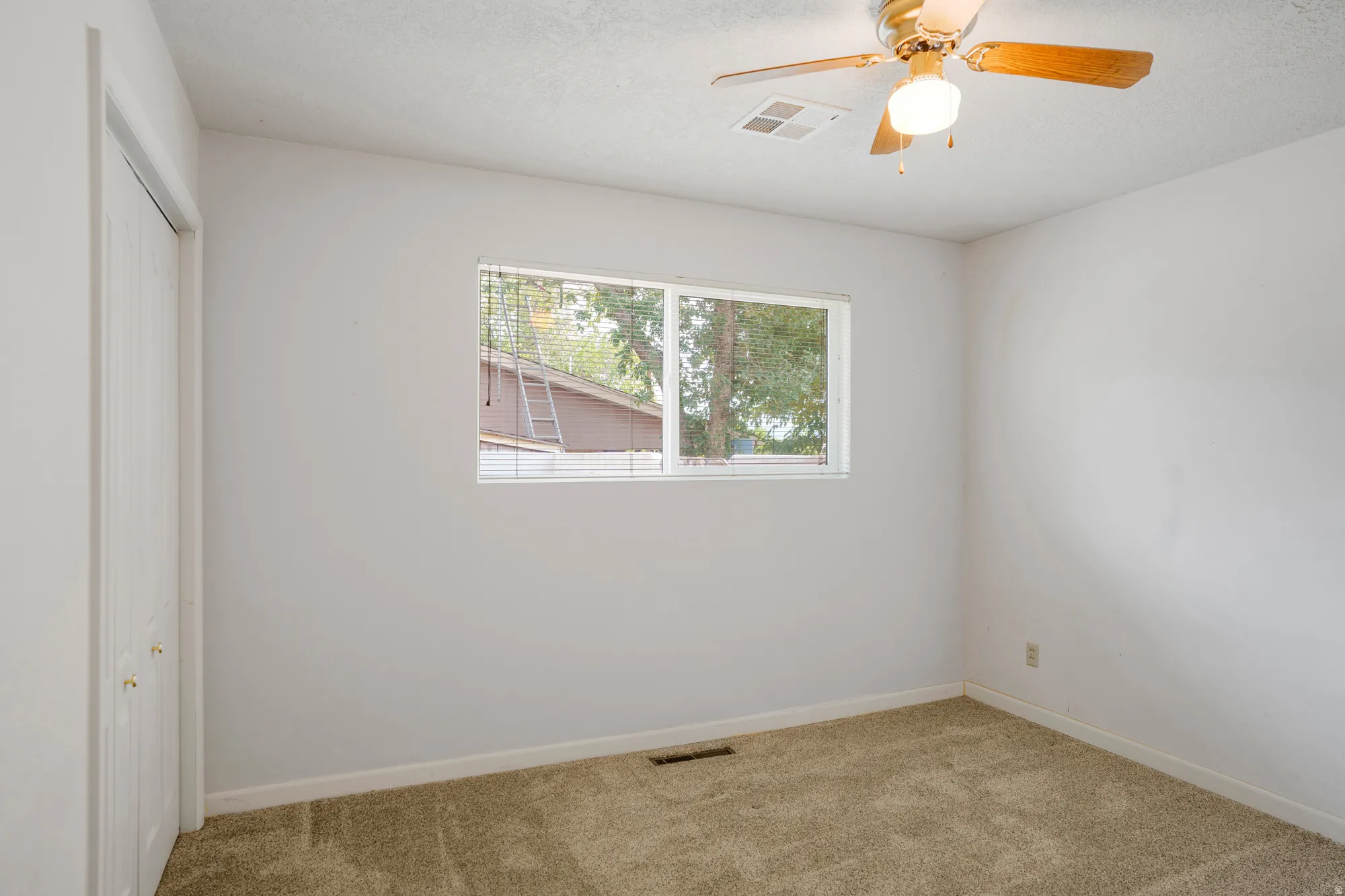 Carpeted room with a single window, a ceiling fan with light, and bi-fold closet doors