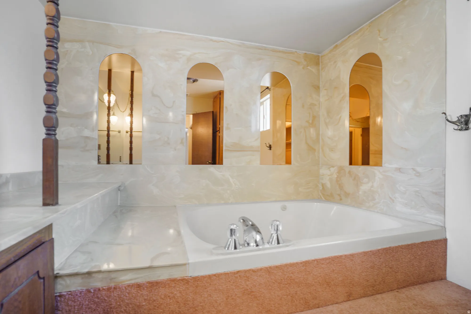 Built-in jetted tub with polished chrome fixtures, surrounded by a light-toned, veined wall and deck