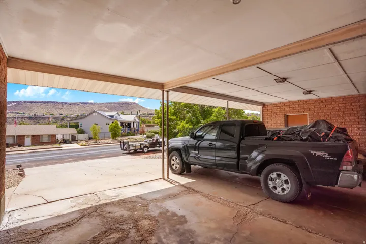 Covered carport with concrete flooring, brick wall, and overhead lighting