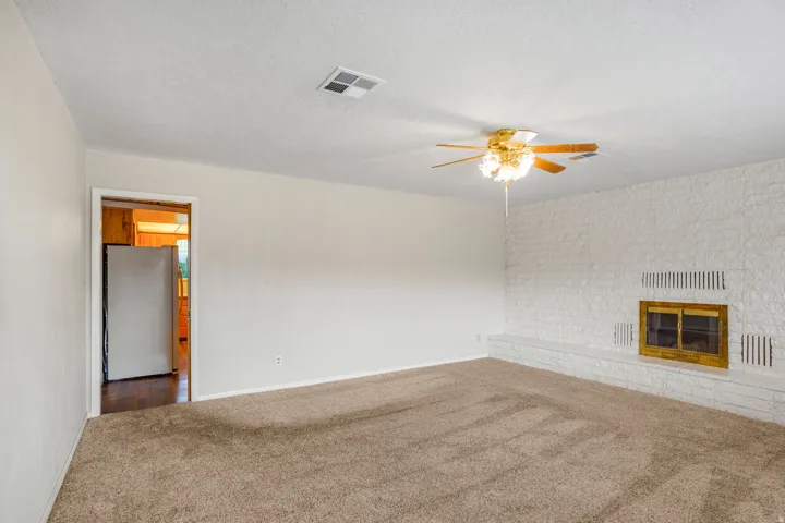 Carpeted living space featuring a white brick fireplace with a wood-framed insert, a ceiling fan with integrated lighting, and a doorway to an adjacent room