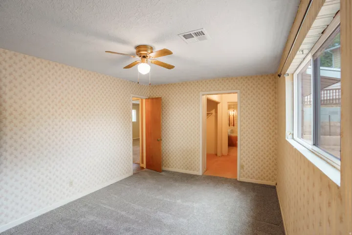 Wall-to-wall carpeting, ceiling fan with integrated lighting, natural wood-finish door, and window with white trim