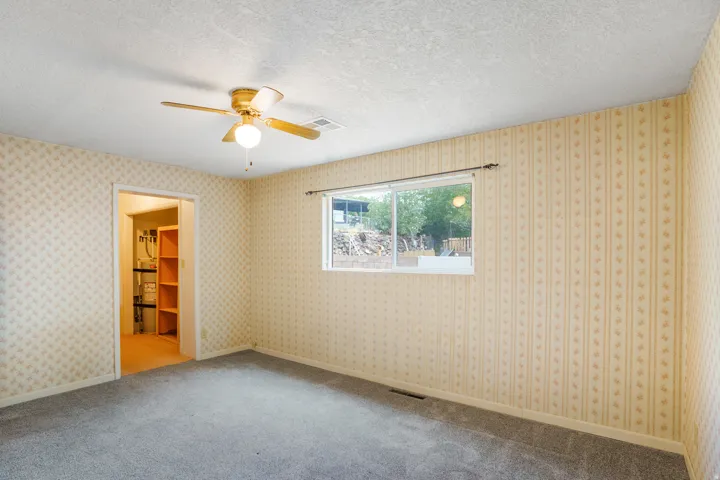 Wall-to-wall carpeting with patterned wallpaper, a single window, and a ceiling fan with integrated lighting