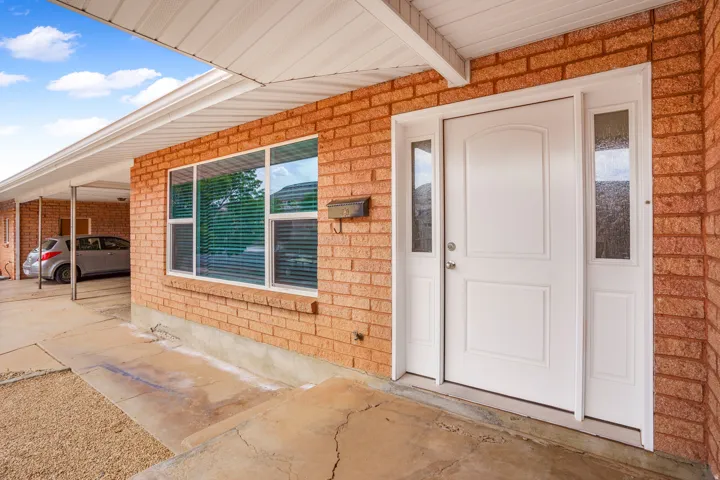 Brick exterior with a white entry door, frosted glass sidelights, and a covered carport