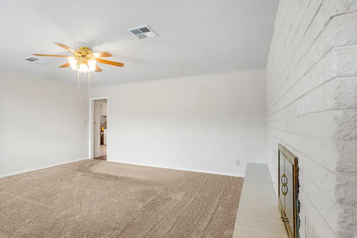 Neutral tone wall paint, textured ceiling, ceiling fan with light fixture, brick fireplace with white finish, and carpeted flooring