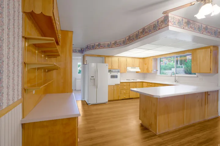 Wood-finish flooring, ample wood cabinetry, extensive countertop space, integrated wall oven, and a double basin sink with a window