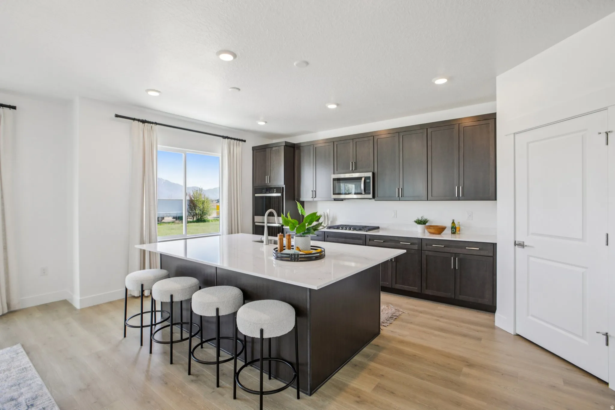 Kitchen featuring wood-finish flooring, dark wood-finish cabinetry, a large kitchen island with a light-toned countertop, recessed lighting, and a built-in microwave