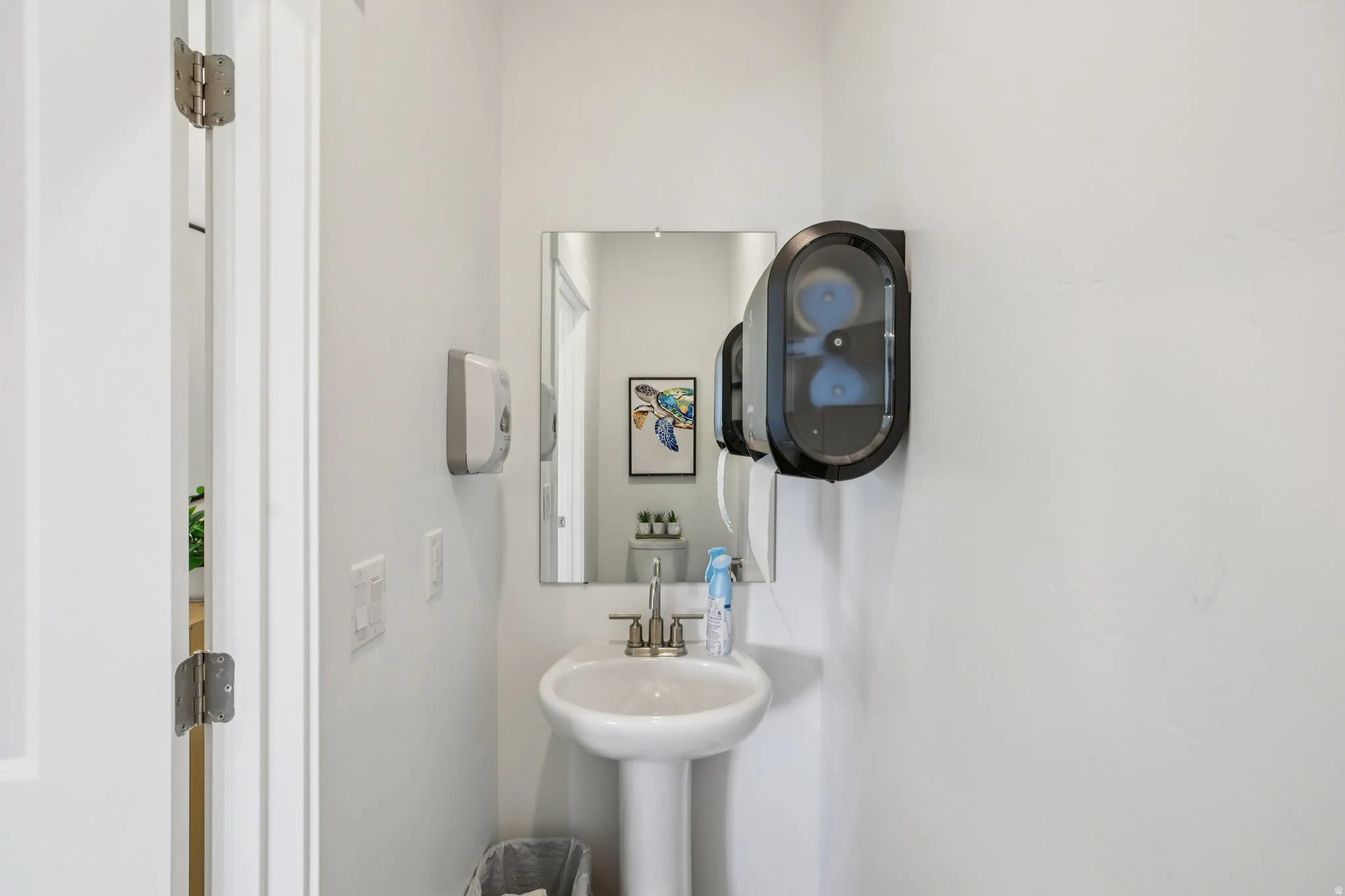 Pedestal sink with a polished chrome faucet, rectangular wall-mounted mirror, and white painted walls