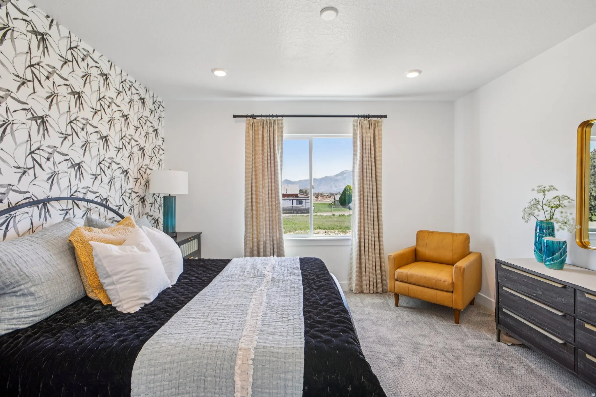 Recessed lighting, a feature wall with patterned wallpaper, soft carpeting, and a window with mountain scenery