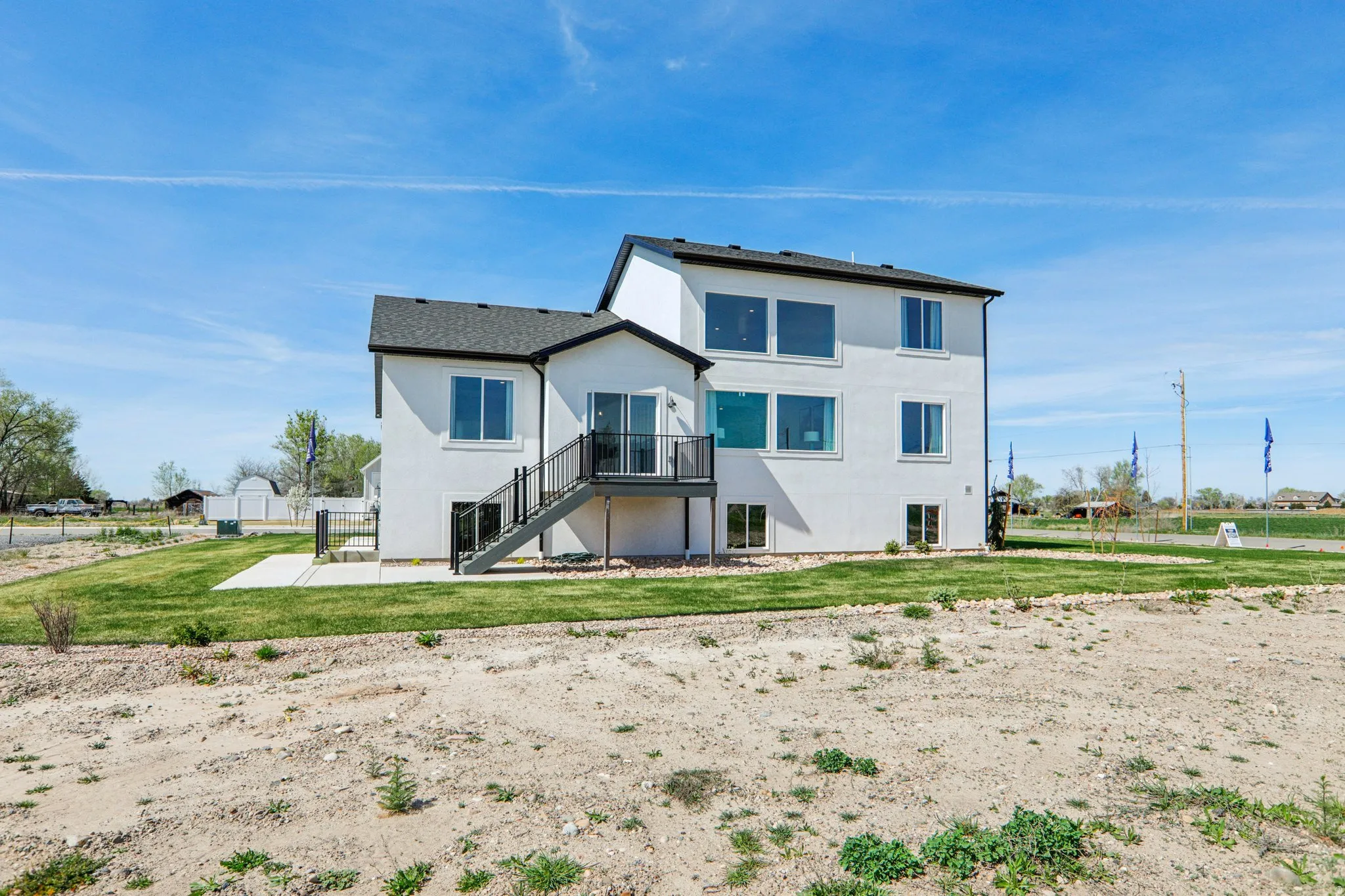 Two-story white stucco exterior with dark trim windows, rear patio, upper deck with black railing, and a sloped shingle roof