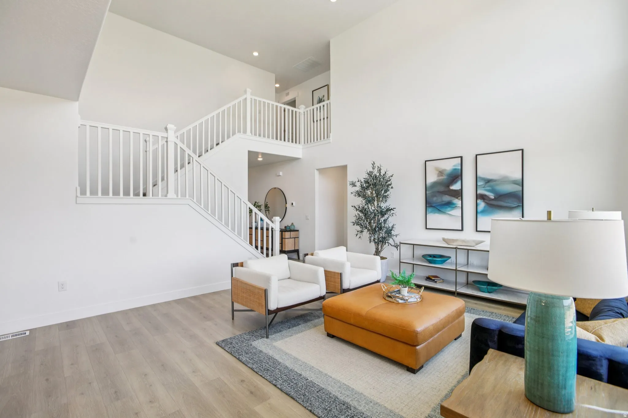Two-story living area with high ceilings, light wood-finish flooring, and a white open staircase with matching railings