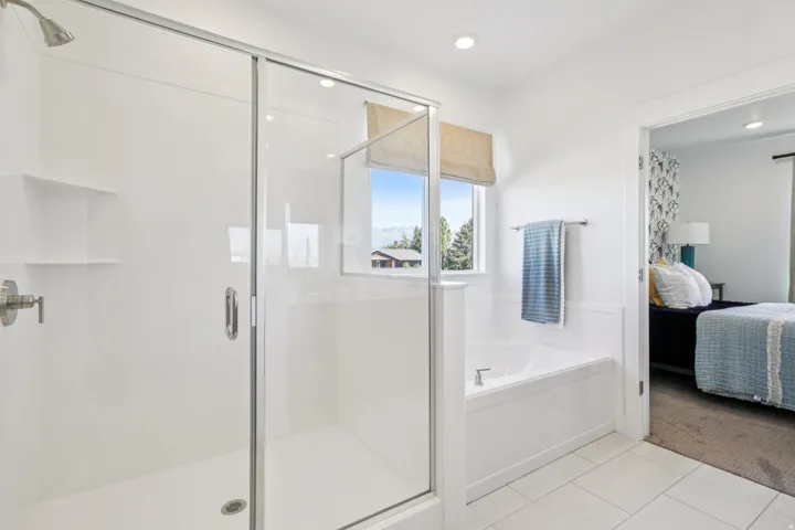White tiled flooring, recessed lighting, built-in bathtub, glass-enclosed shower, and a large window