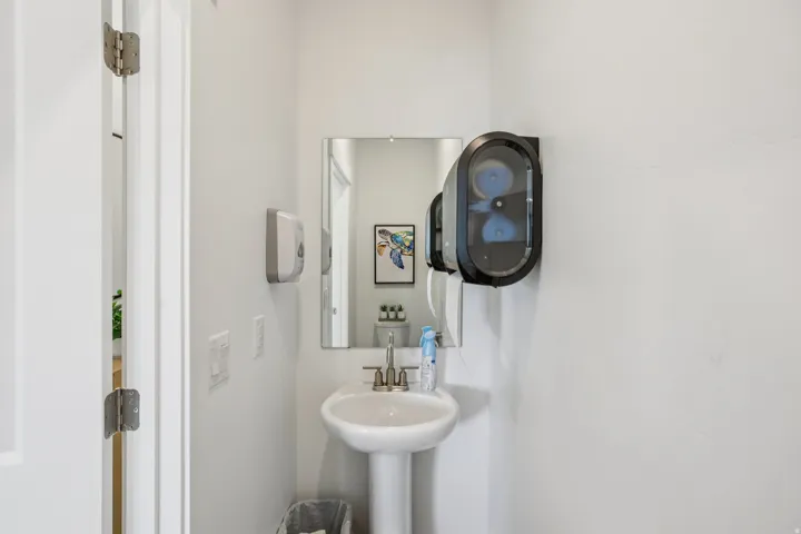Pedestal sink with a polished chrome faucet, rectangular wall-mounted mirror, and white painted walls