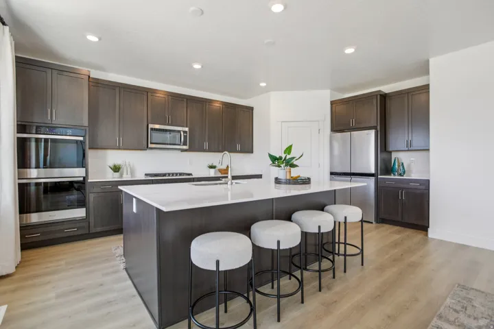 Kitchen featuring wood-finish flooring, recessed lighting, a central island with white countertop, dark wood-finish cabinetry, and stainless steel appliances