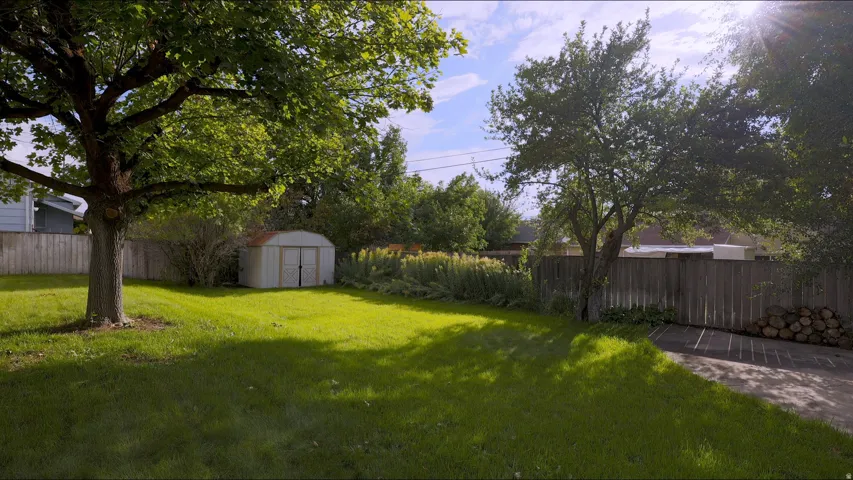 Expansive lawn area, mature trees, wood fence enclosure, detached storage shed, and paved surface