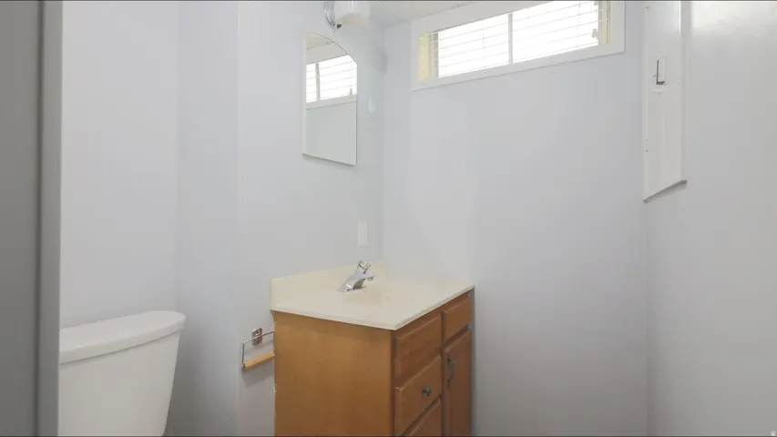 White toilet, wood-finish vanity with countertop, wall-mounted mirror, and horizontal window