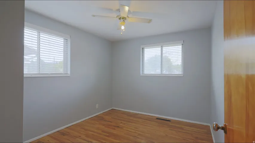 Hardwood flooring, two windows with blinds, ceiling fan with integrated lighting, and a wood-finish door
