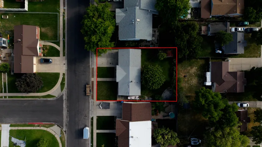 Aerial perspective showcasing a property with a paved driveway, a gabled roof, and a green lawn
