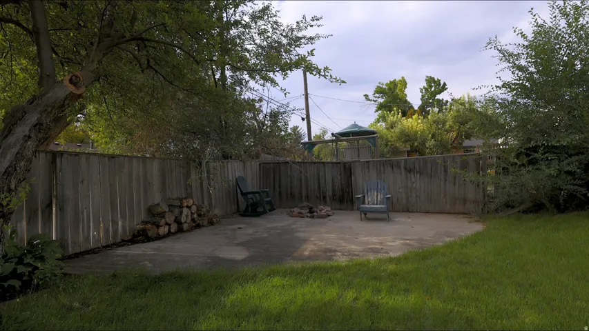 Expansive backyard featuring a concrete patio, a stone fire pit, a wood privacy fence, and mature trees