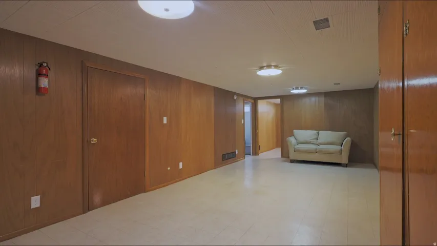 Spacious room featuring wood-paneled walls, light-colored flooring, and ceiling-mounted lighting fixtures