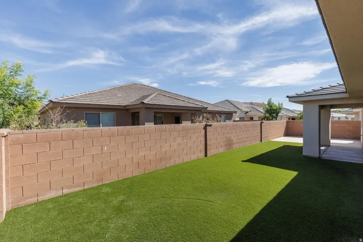 Expansive backyard featuring artificial turf, a block privacy fence, and a covered concrete patio