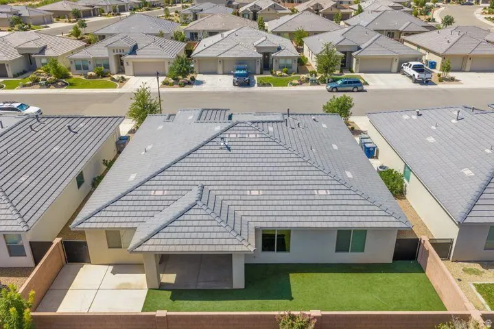 Pitched roof with gray tile, rear patio with concrete slab, artificial turf lawn, and perimeter fencing