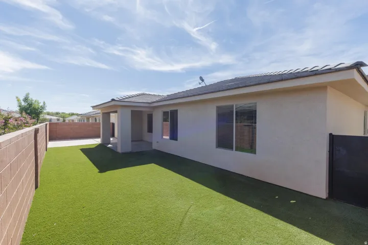 Expansive backyard featuring artificial turf, a covered patio, stucco exterior, and privacy fencing