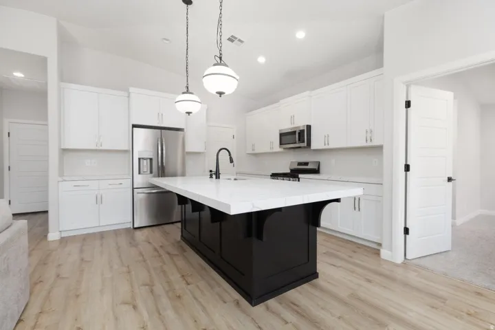 Modern kitchen featuring white cabinetry, stainless steel appliances, a large black island with a white countertop, and wood-finish flooring