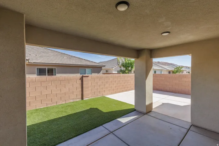 Covered patio with integrated lighting, extending to a concrete paver area and a section of artificial turf, enclosed by block walls