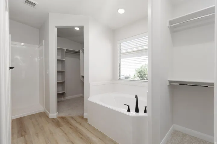 Corner soaking tub with matte black fixtures, wood-finish flooring, walk-in shower, window with blinds, and recessed lighting