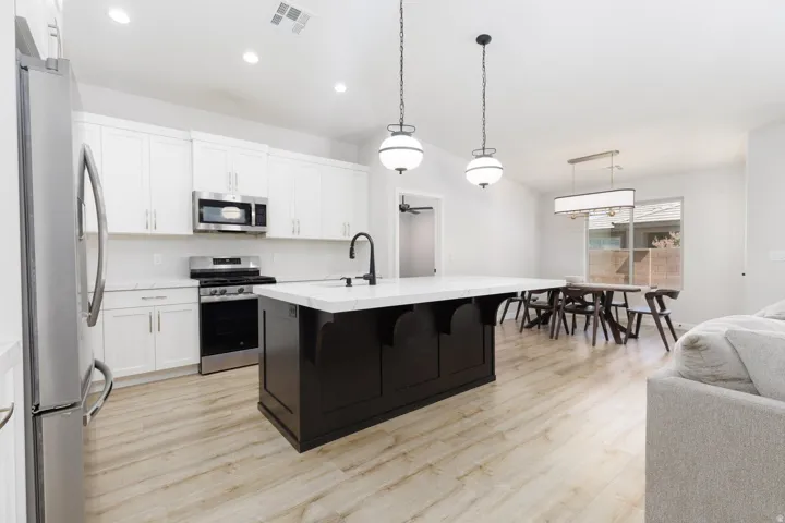Kitchen featuring a dark-tone center island with a light-tone countertop, stainless steel appliances, white cabinetry, and wood-finish flooring