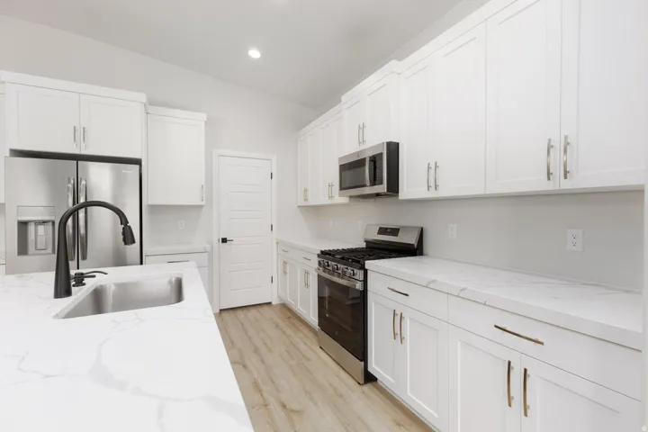 Kitchen featuring white cabinetry, stainless steel appliances, wood-finish flooring, a stainless steel sink with a matte black faucet, and white countertops with veining
