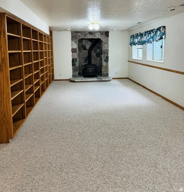 Built-in wood shelving, stone fireplace surround, wood-burning stove, and neutral-toned carpeting