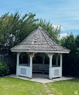Outdoor gazebo featuring a shingle roof and white lattice detailing, set on a concrete pad with a stone path