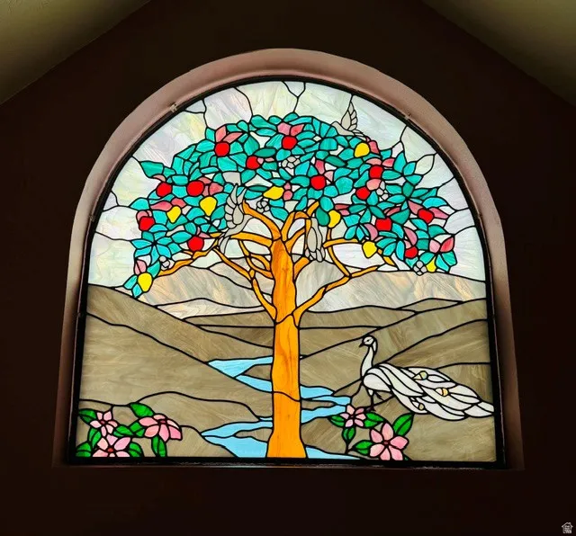 Arch-top stained-glass window featuring a tree, birds, peacock, and floral elements