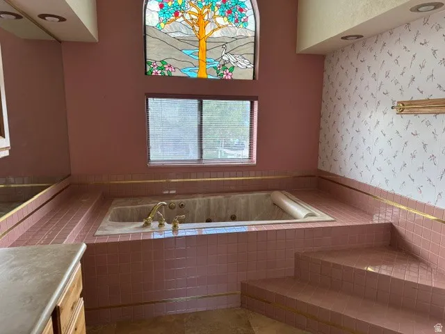 Jetted soaking tub with brass fixtures, surrounded by pink tile and gold trim