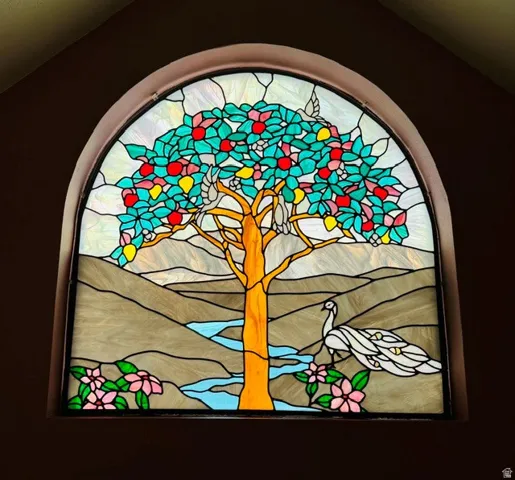 Arch-top stained-glass window featuring a tree, birds, peacock, and floral elements