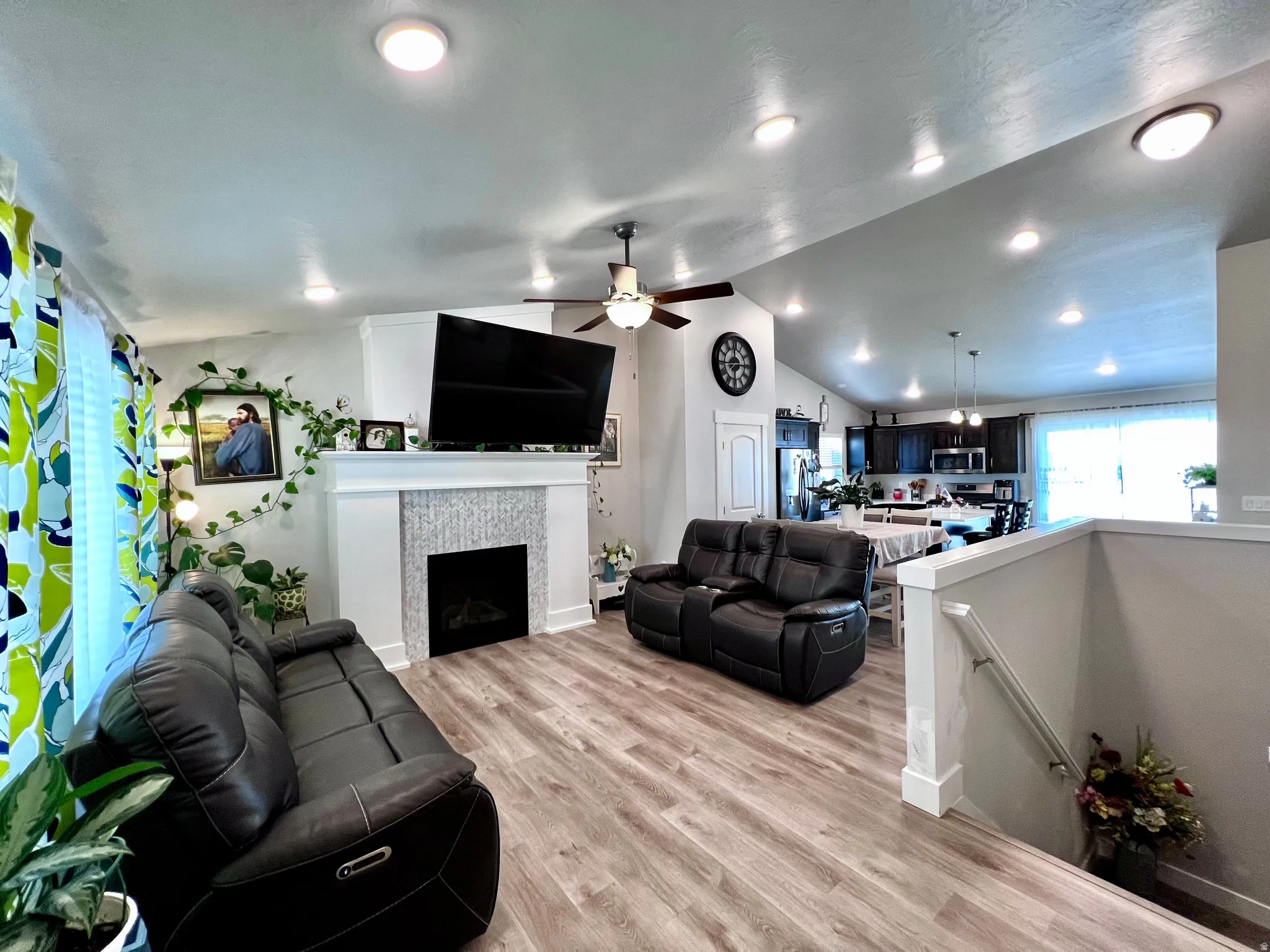 Vaulted ceiling with recessed lighting, wood-finish flooring, fireplace with tiled surround, and open kitchen concept with dark wood cabinetry