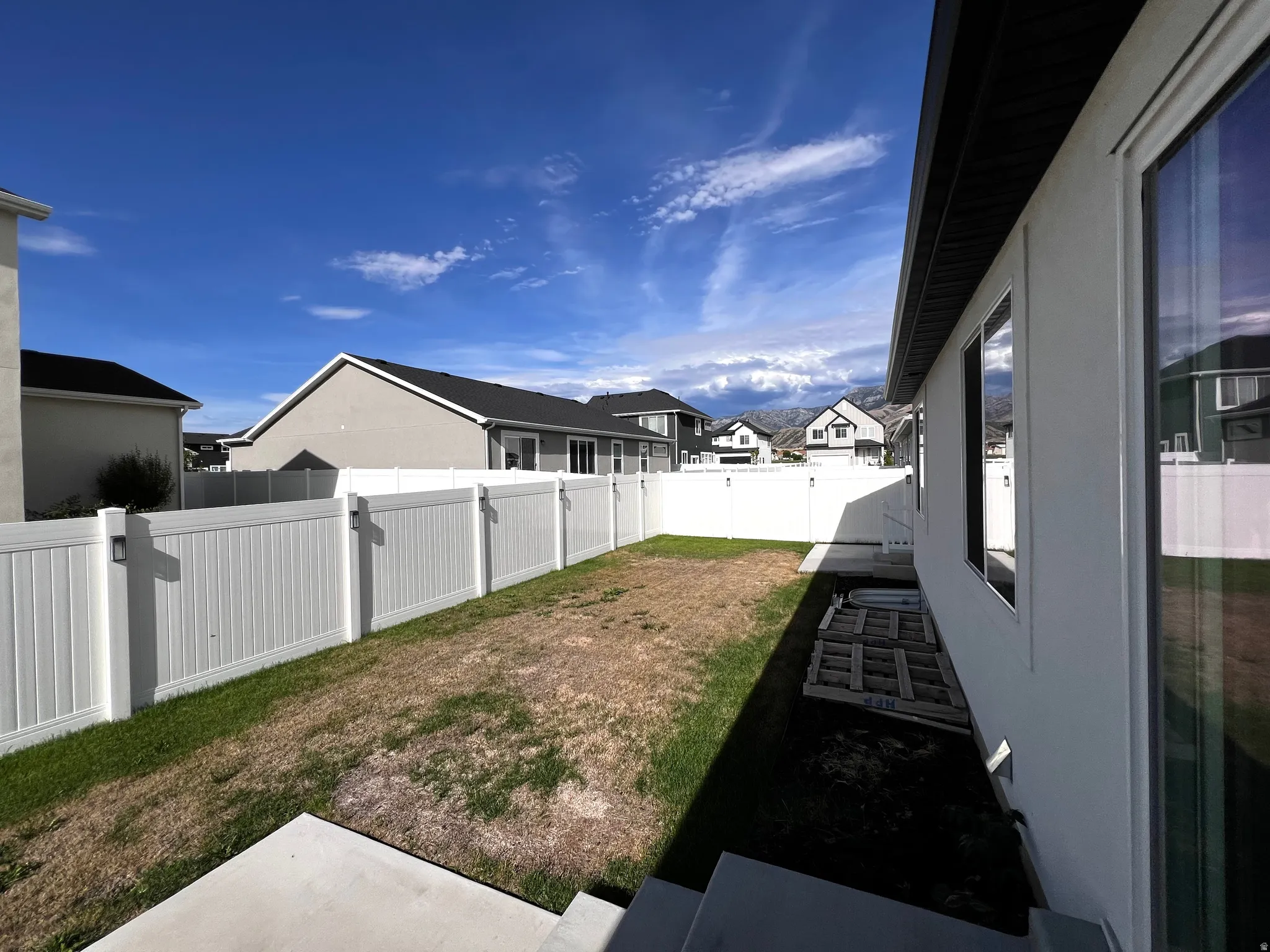 Enclosed backyard featuring a white privacy fence, concrete patio, and exterior windows