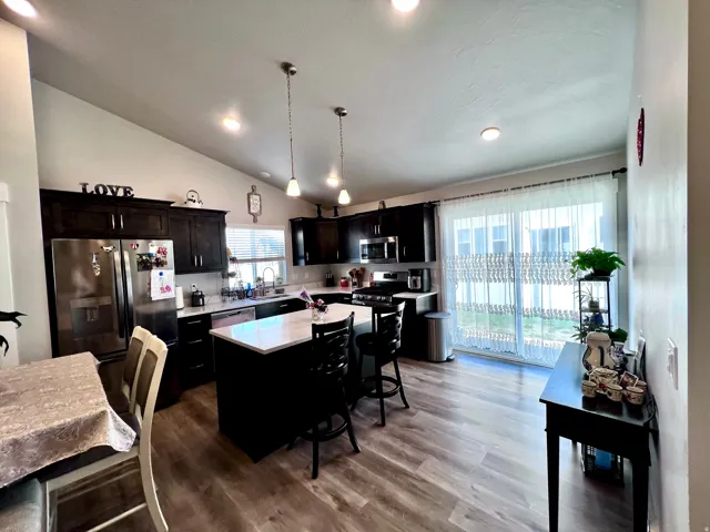 Kitchen featuring dark wood cabinetry, stainless steel appliances, a center island with white countertop, wood-finish flooring, and a sliding glass door