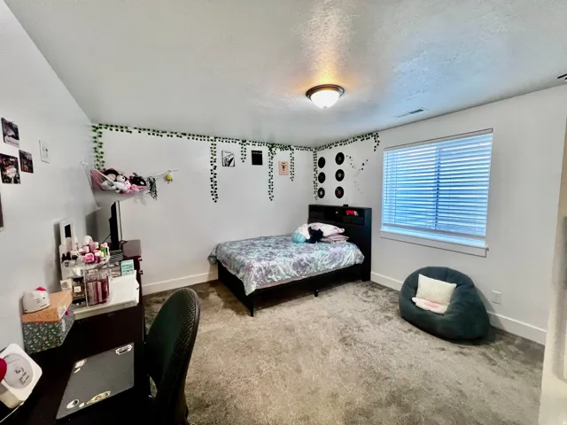 Basement apartment bedroom. White walls with contrasting trim, a window with horizontal blinds, a built-in ceiling light fixture, and carpeted flooring