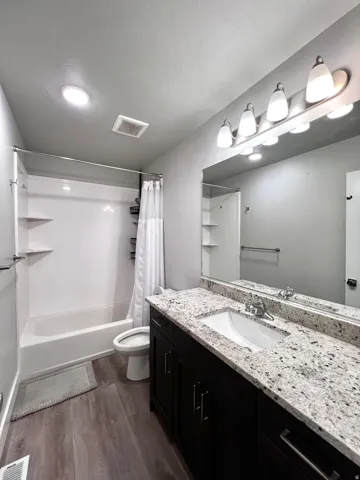 Bathroom featuring a dark wood-finish vanity, light speckled countertop with integrated sink, wood-finish flooring, and a shower/tub combination