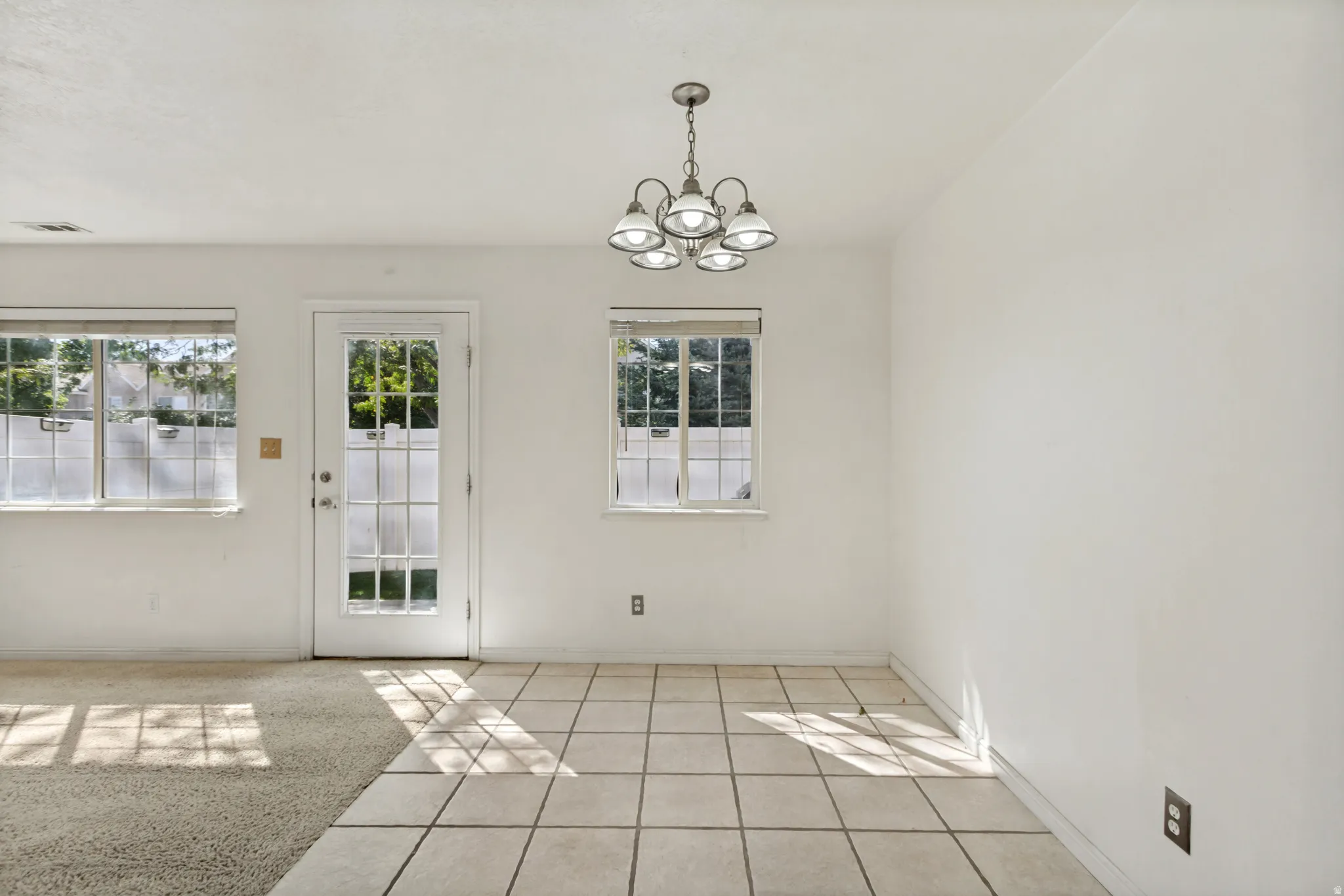 Tile flooring, carpeting, white walls, multiple windows, and a glass-paneled door