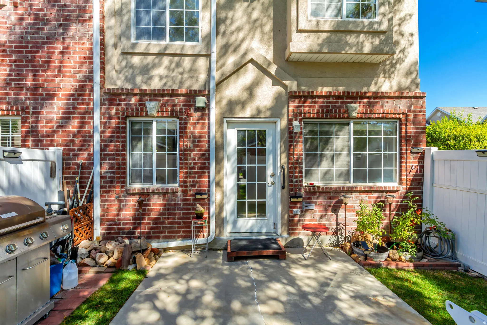 Patio with a white privacy fence, brick and stucco exterior, and white-framed windows