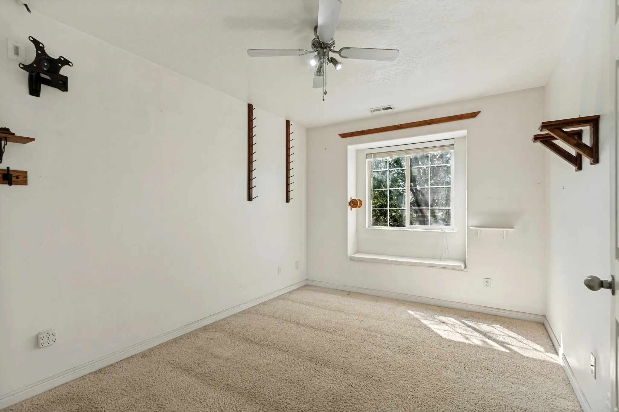 Carpeted room featuring a ceiling fan with integrated lighting, a window with a sill, and built-in wall shelving