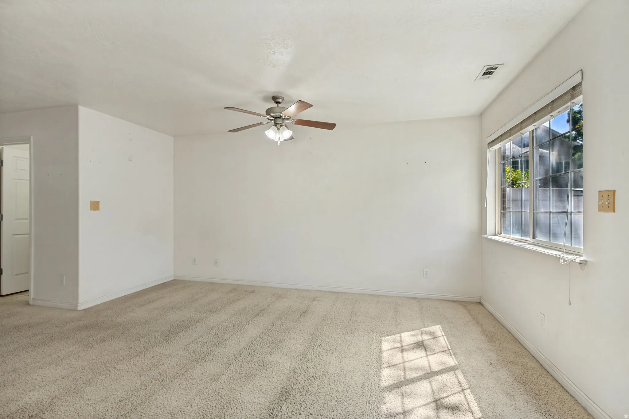 Spacious room with plush carpeting, a large window, and a ceiling fan