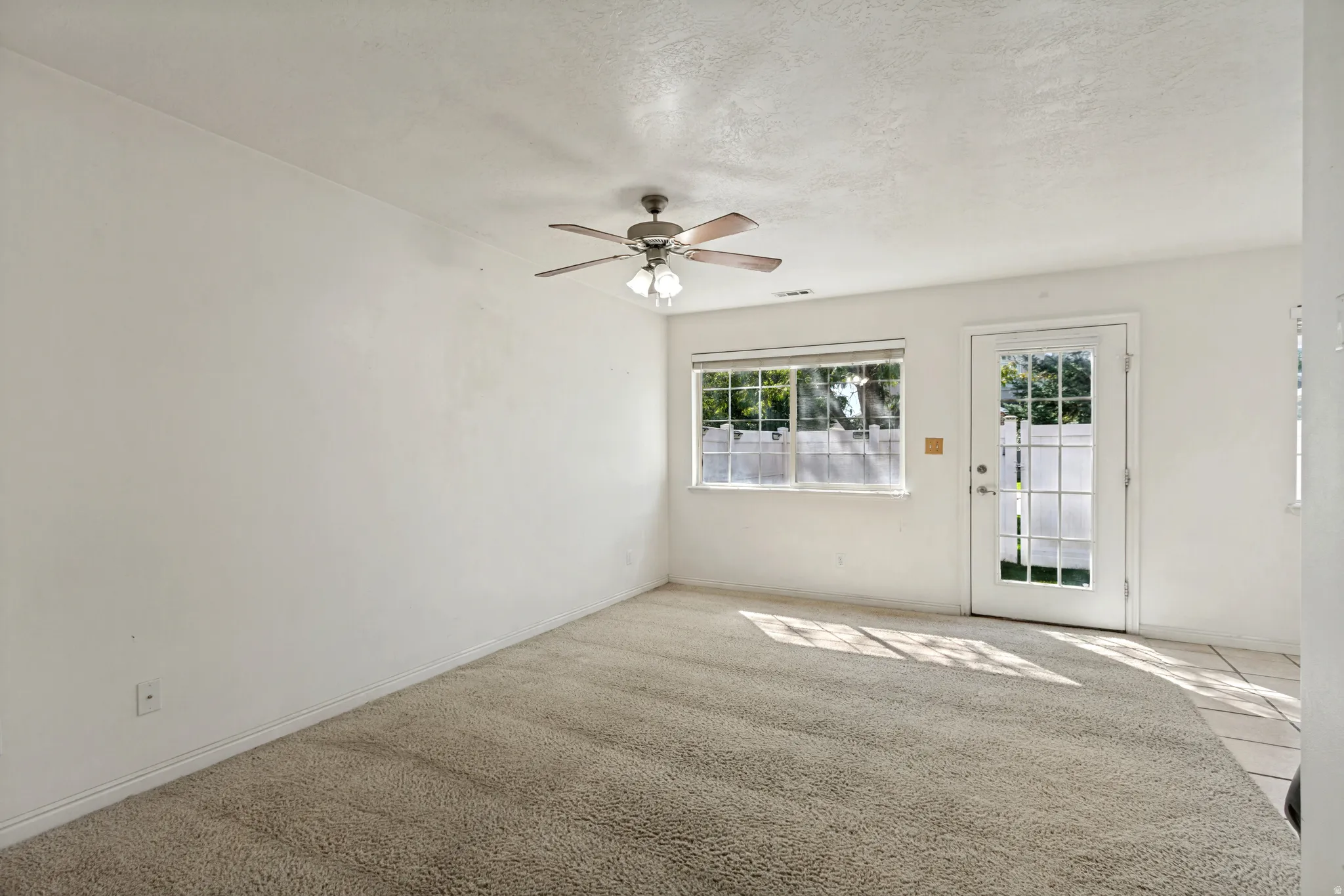 Carpeted flooring, ceiling fan with light fixture, multiple windows, and a glass-paneled exterior door