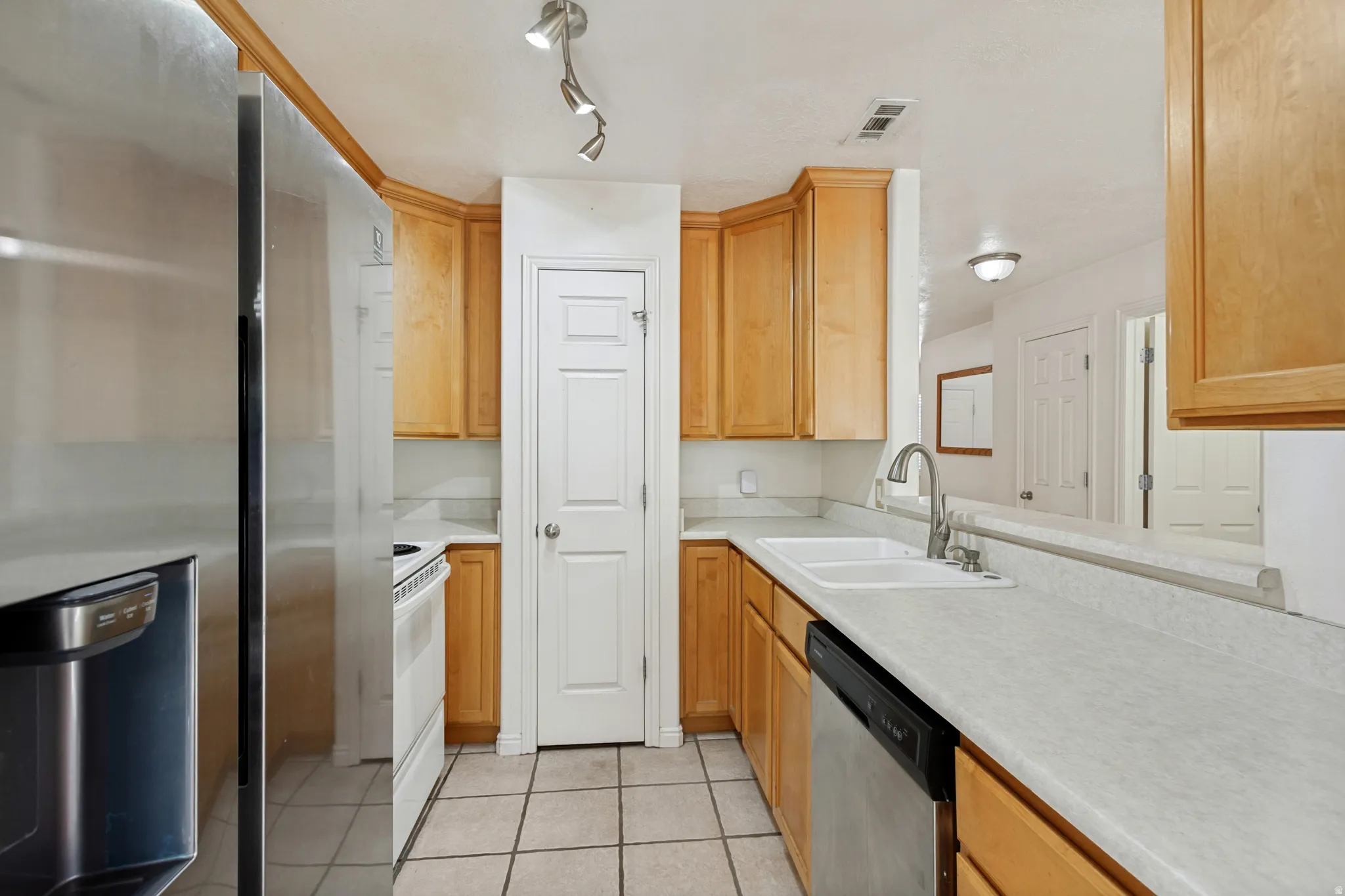 Stainless steel refrigerator, wood cabinetry, tile flooring, dual-basin sink, and track lighting