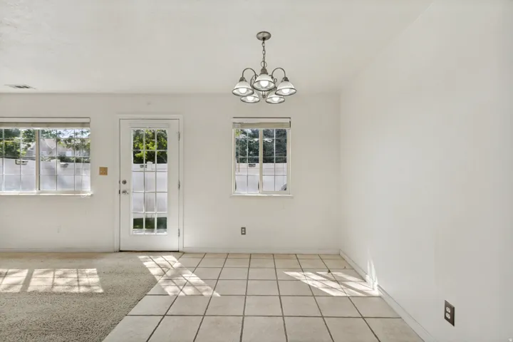 Tile flooring, carpeting, white walls, multiple windows, and a glass-paneled door